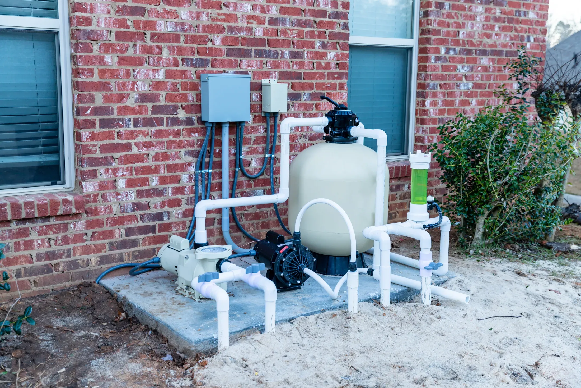 A residential pool equipment pad with a newly plumbed pump and sand filter beside a brick wall